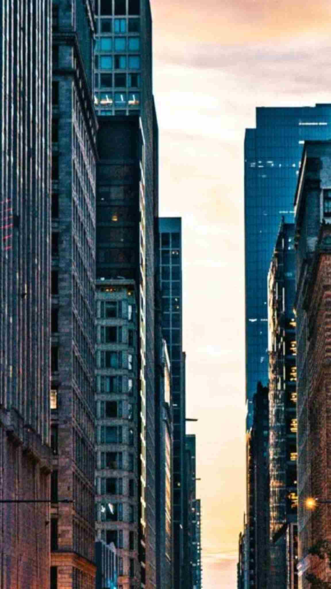 Tall city buildings frame a narrow street under a pale evening sky